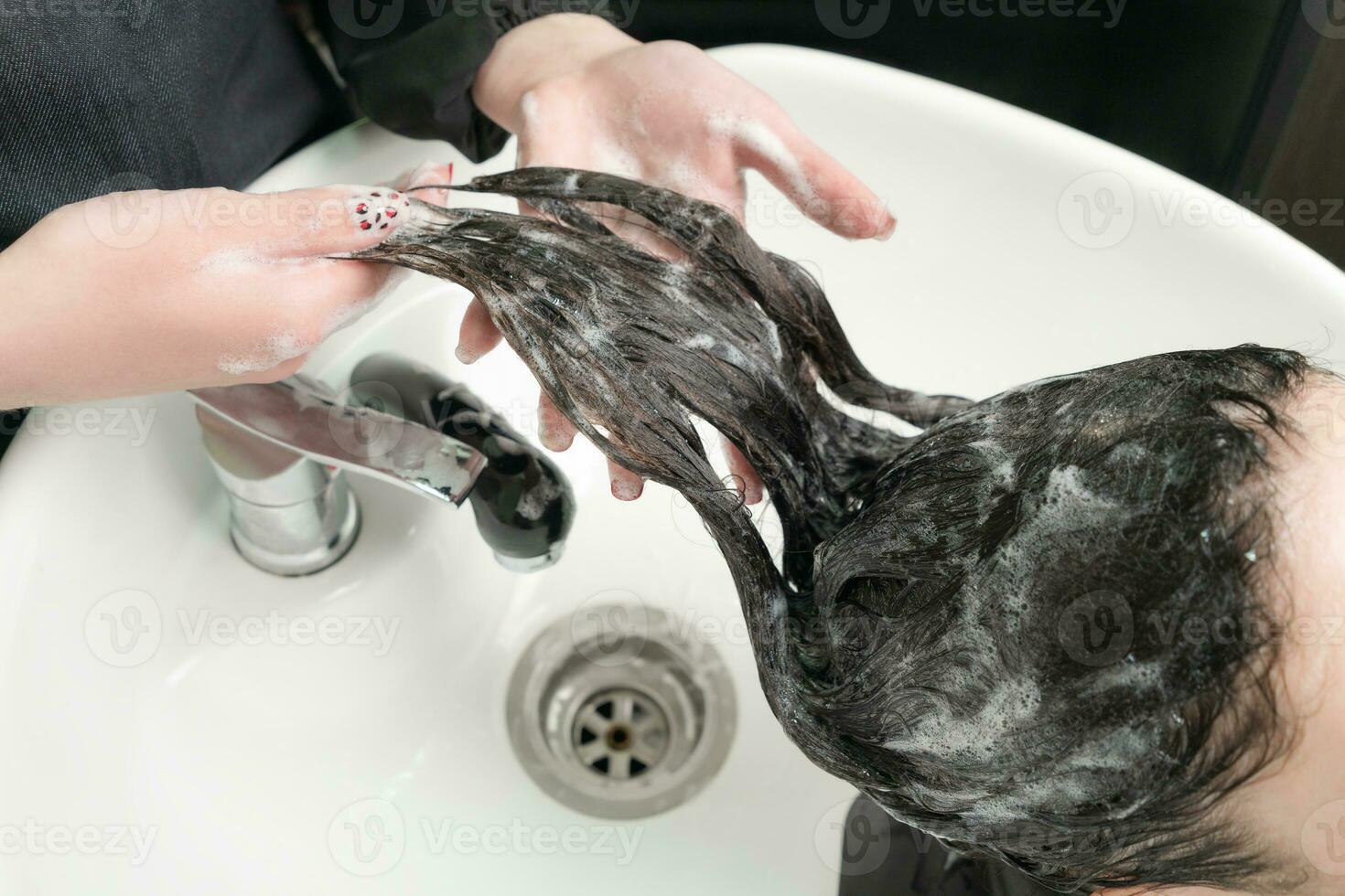 Hairstylist wash long hair of brunette woman with shampoo in special sink for shampooing photo