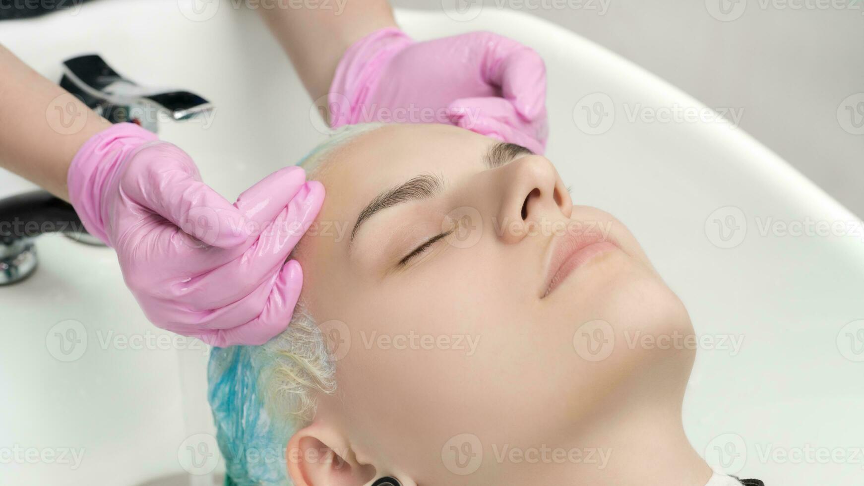 Hairstylist hands in pink gloves washing hair of young woman in professional beauty salon photo