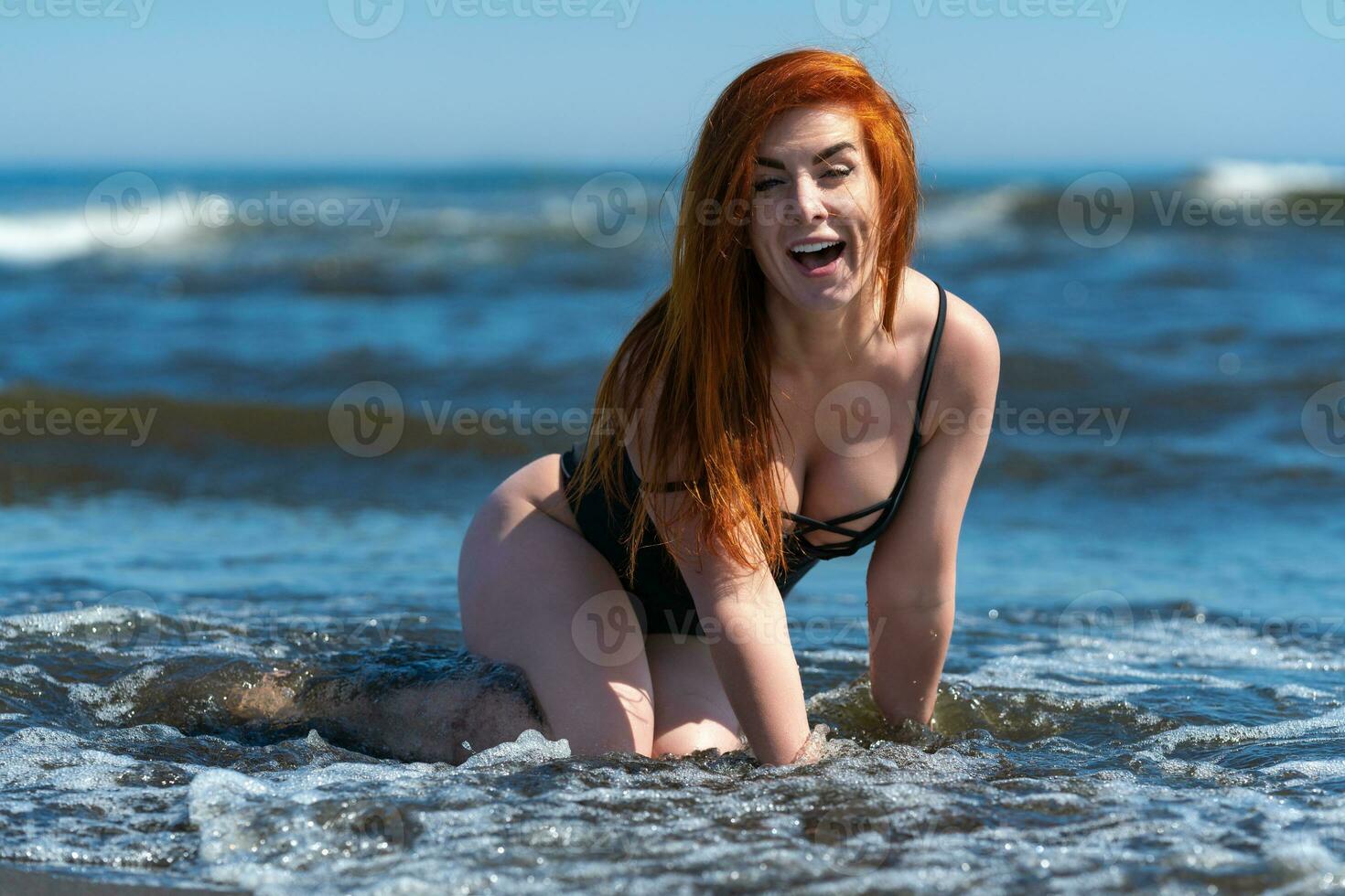 Enthusiastic redhead woman in swimsuit in breaking sea waves of surf during summer beach holiday photo