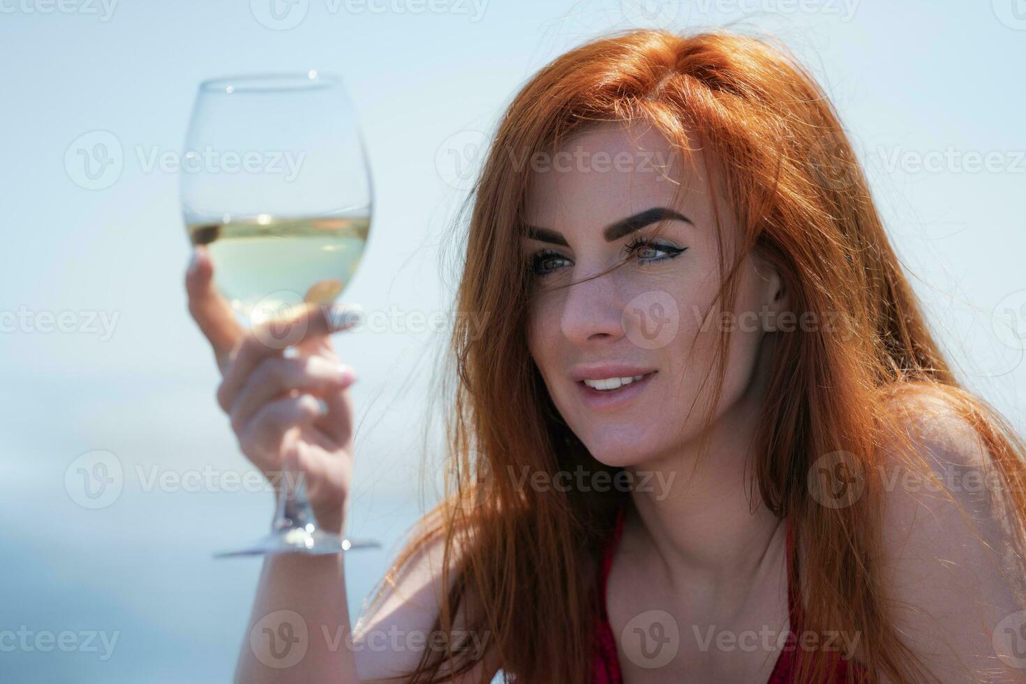 de cerca retrato contento pelirrojo mujer elevado vaso de vino a ojo nivel y es mirando atentamente a eso foto