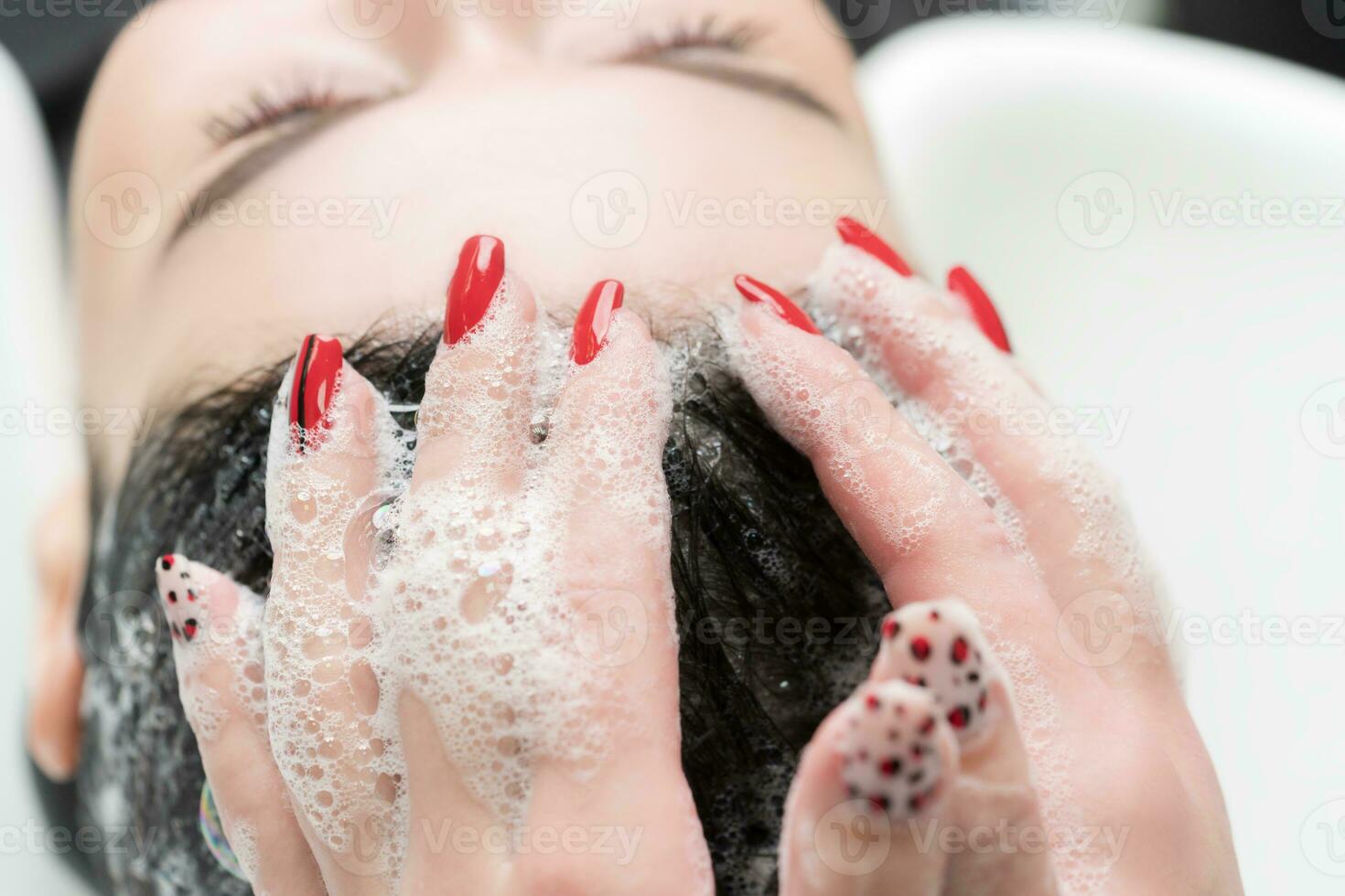 Hairdresser's hands wash hair of brunette woman with shampoo in special sink for shampooing photo