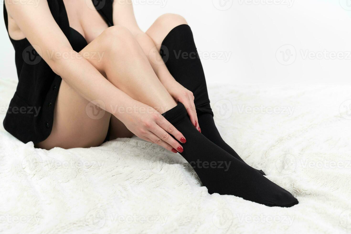 Cropped view of woman carefully dressing black tights over her legs. Unrecognizable female on bed photo