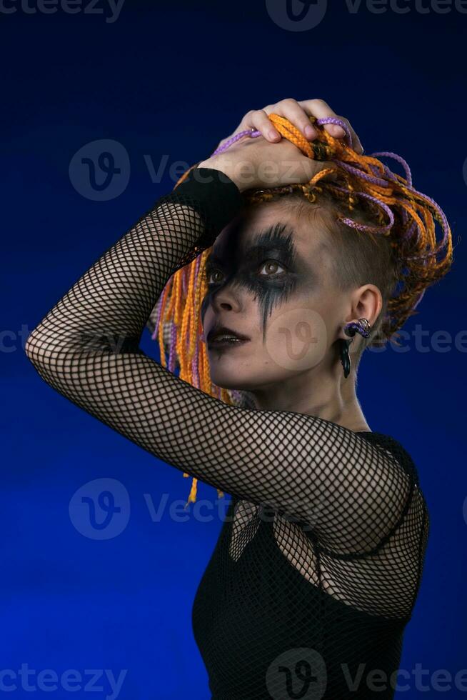 Young female with orange color braids hairdo and horror black stage makeup painted on face photo