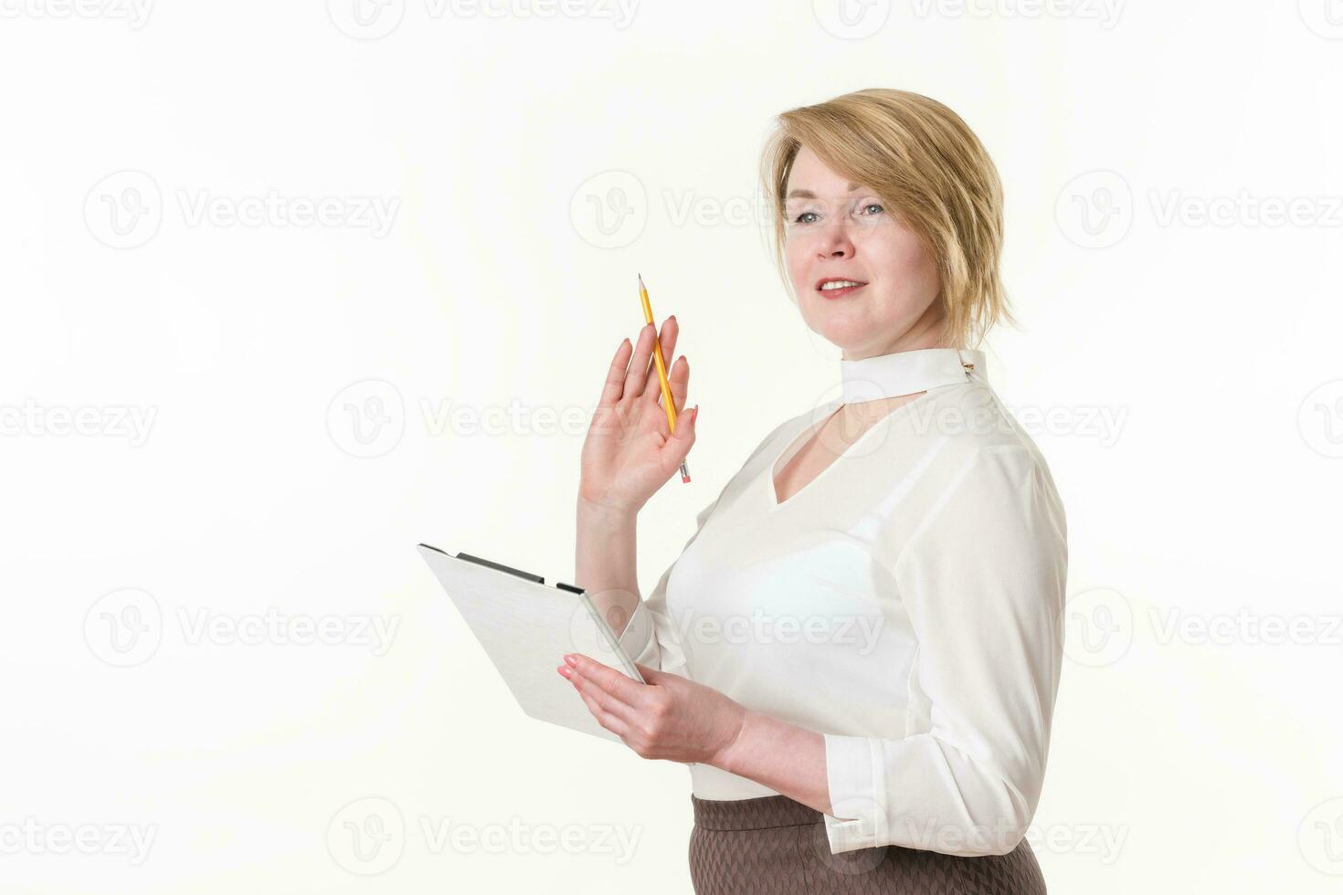 Blonde woman wearing in white blouse holding clipboard and pencil in hands, looking away and smiling photo