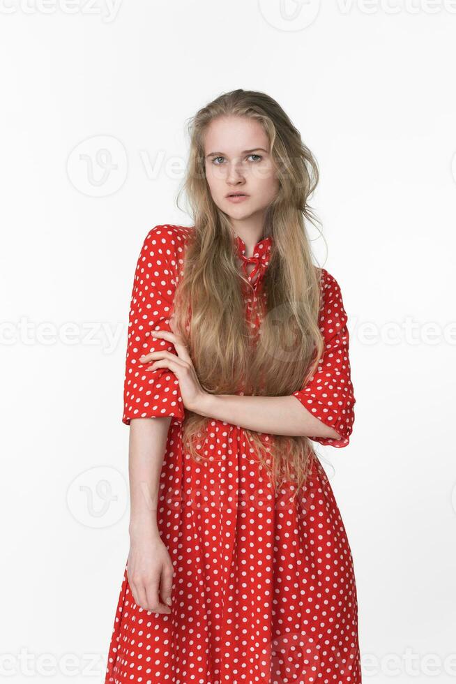 Fashionable blonde woman with long hair dressed in summer polka dot dress poses on white background photo