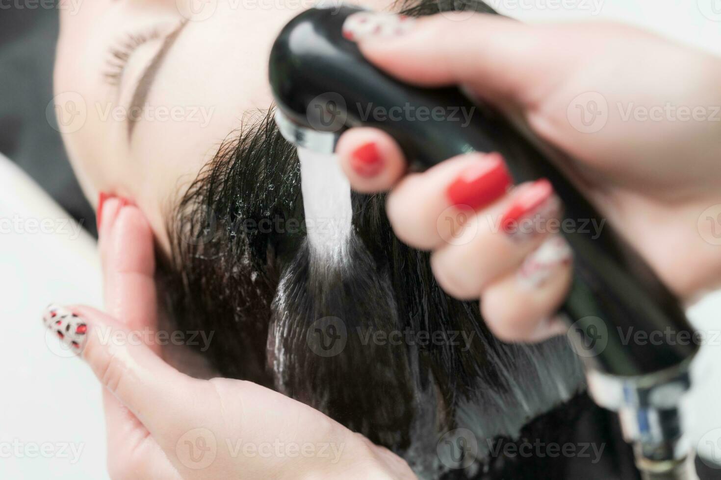 Hands of hairdresser wash hair of brunette with shampoo and shower water in in beauty salon photo