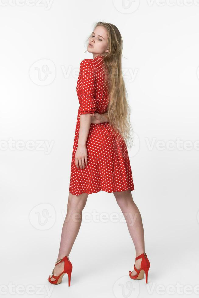 Stylish blonde woman in summer red polka dot dress looking down, standing on white background photo