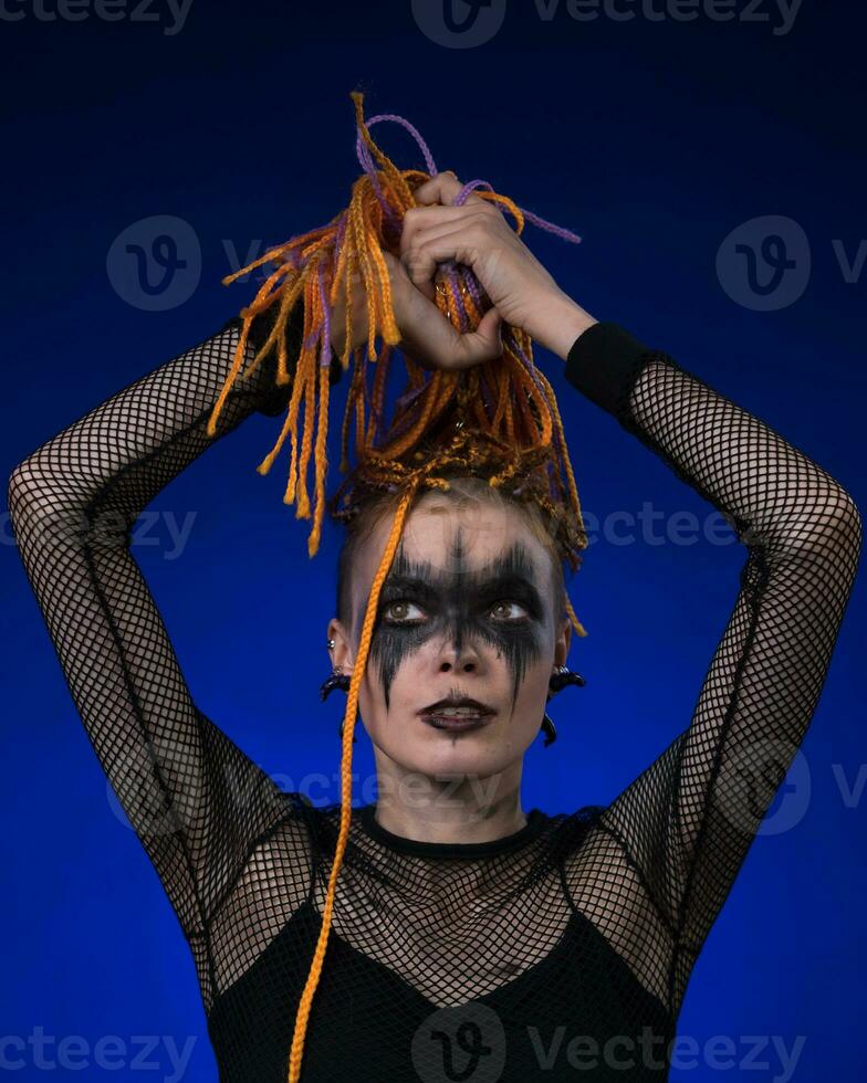 Informal young female with colored braids hairdo and spooky black stage makeup painted on face photo