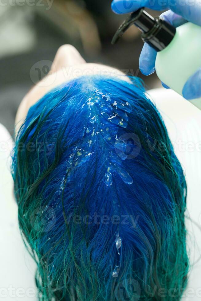 Hairdresser applies shampoo to client's blue hair for washing after process of coloring hair in dark blue color photo