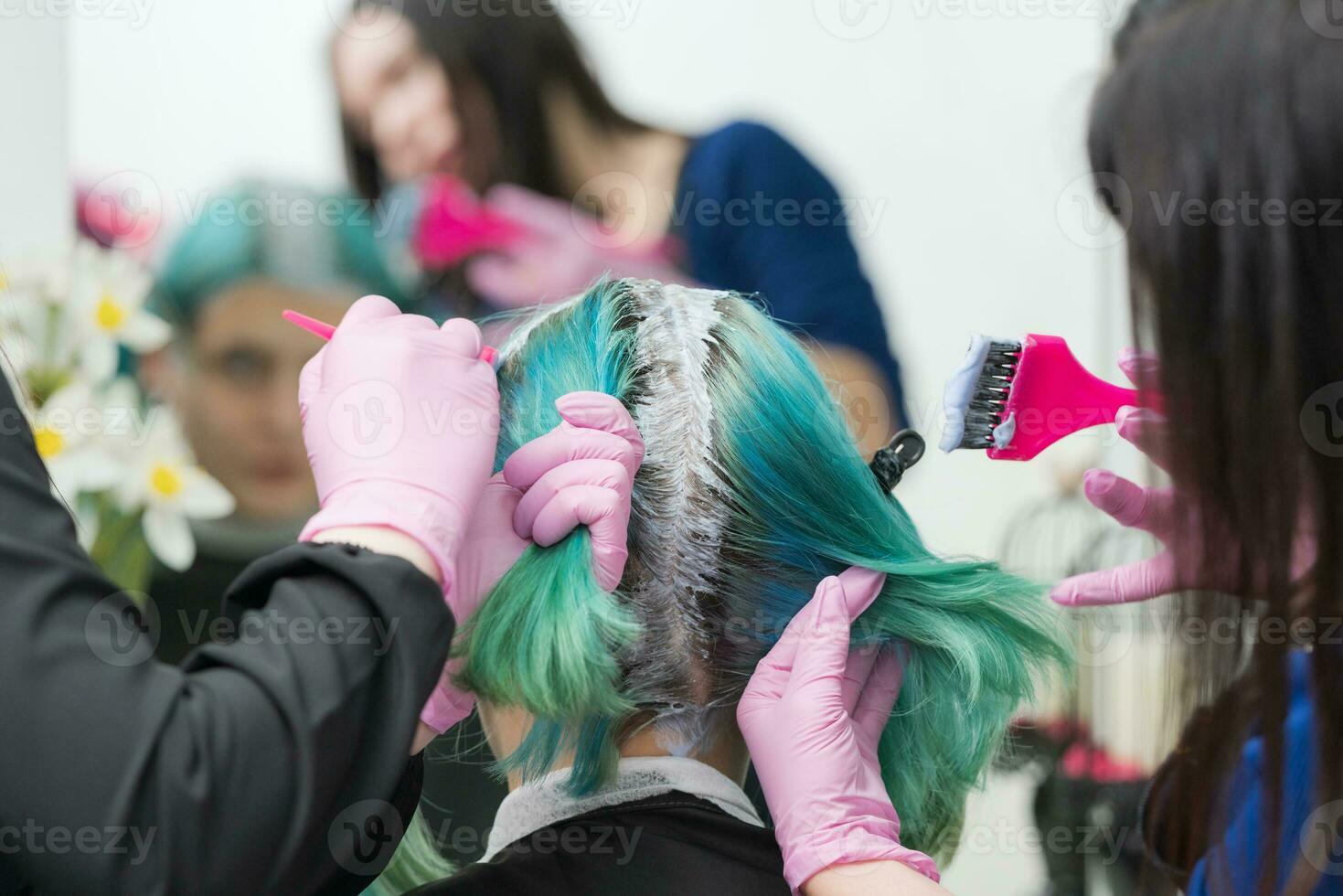 Process of hair dyeing in beauty salon. Two hairdressers applying paint to hair during bleaching hair roots photo