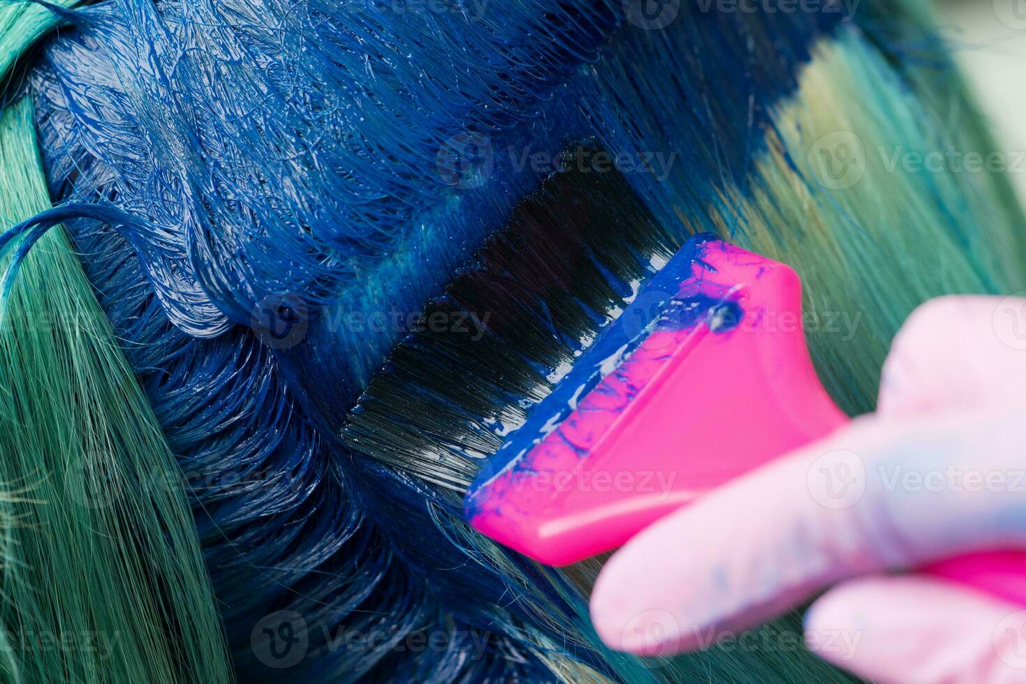 Close-up of hair coloring at beauty salon. Hairdresser using pink brush while applying blue paint to female during dyeing hair in unique color photo