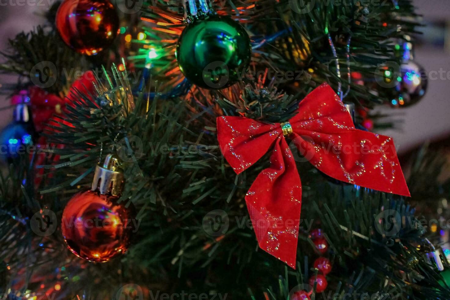 New Year's toys on the Christmas tree. Christmas tree decorations close-up. Garlands, red and green balloons, bows on a green pine tree. Christmas atmosphere at home, background for holiday cards photo