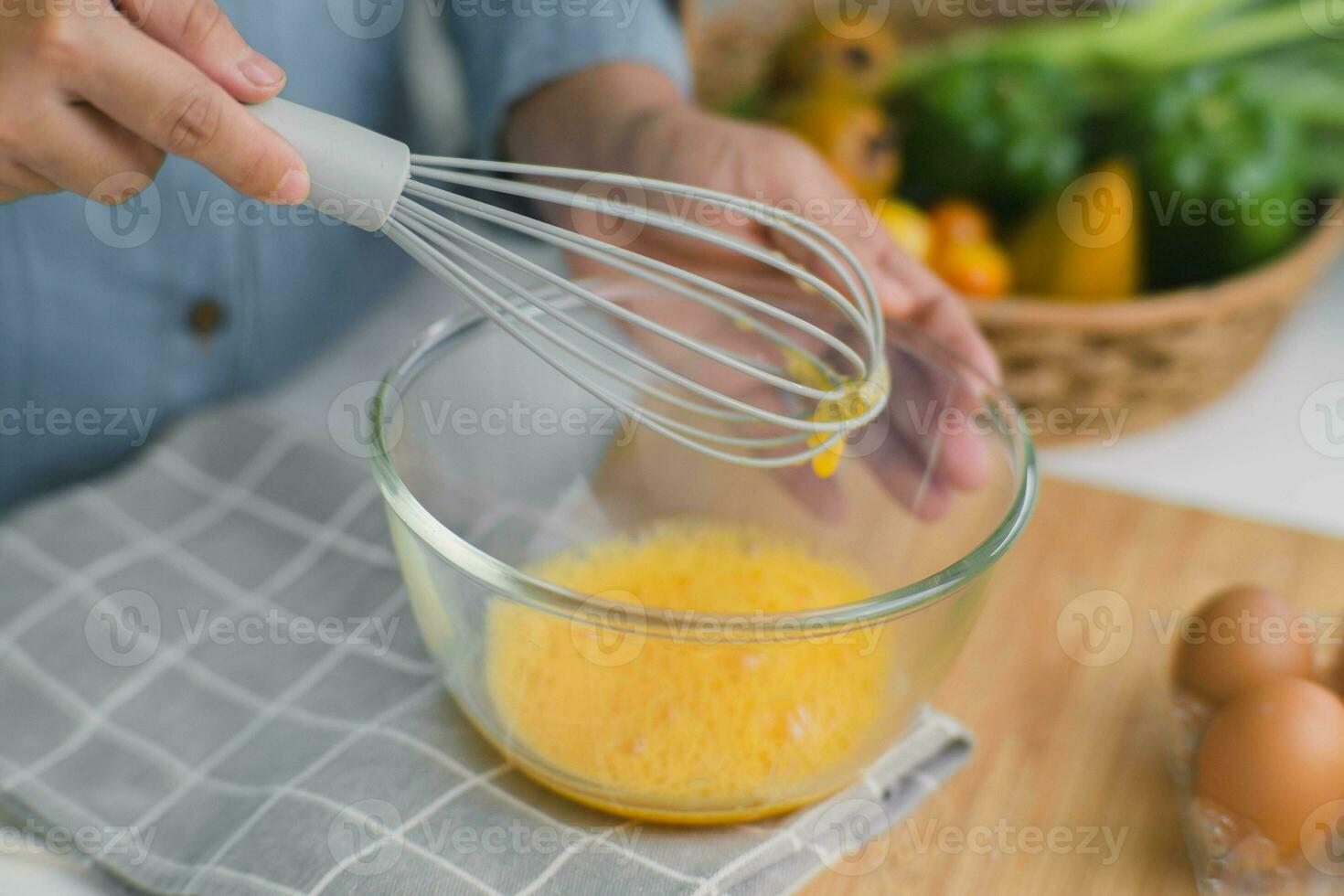 joven mujer Cocinando en brillante cocina, manos batir huevos en un cuenco metido en toalla y de madera mesa. preparando ingredientes para sano cocinando. hecho en casa comida foto