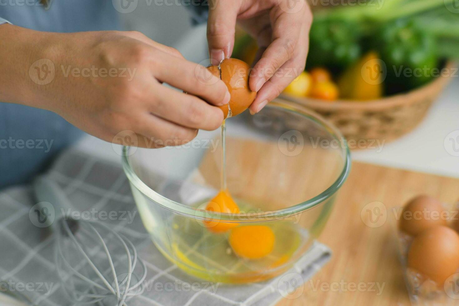 Young woman cooking in a bright kitchen, hand made cracked fresh egg yolks dripping into the bowl. Preparing ingredients for healthy cooking. Homemade food photo