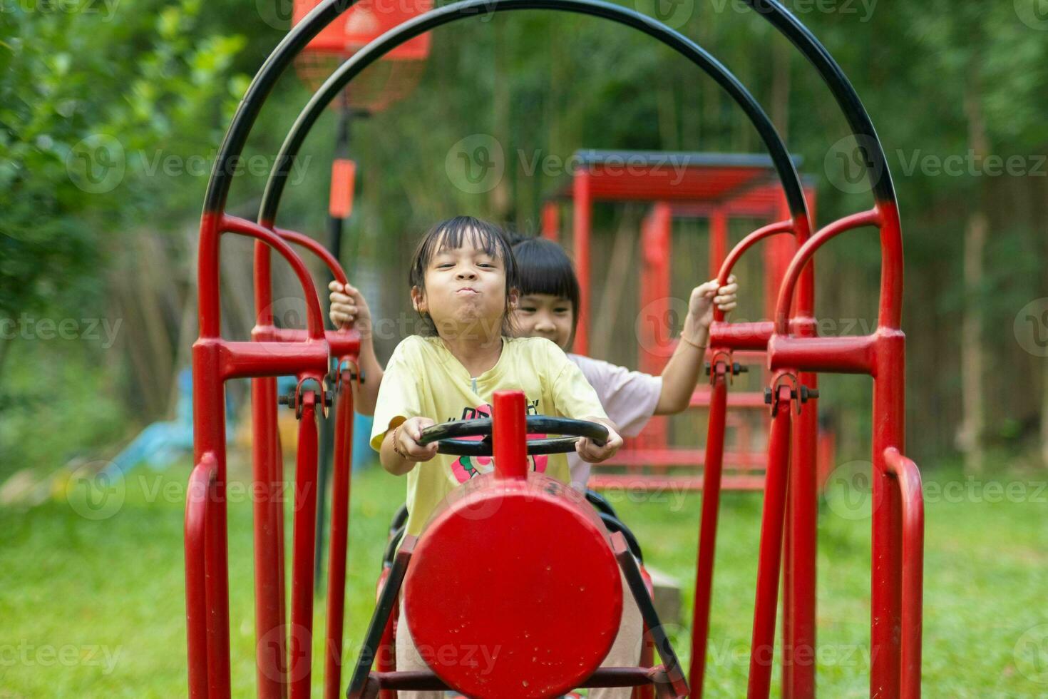 Two little girl playing at outdoor playground. Active children play on colorful trains in the park. Healthy summer activity for children. photo