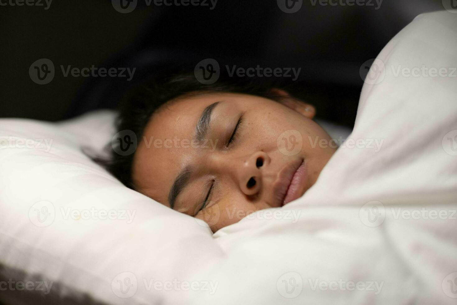 Asian woman resting covered with blanket on white sheets in bedroom. Woman sleeping. Peaceful woman lying in bed and keeping eyes closed while covered with blanket. photo