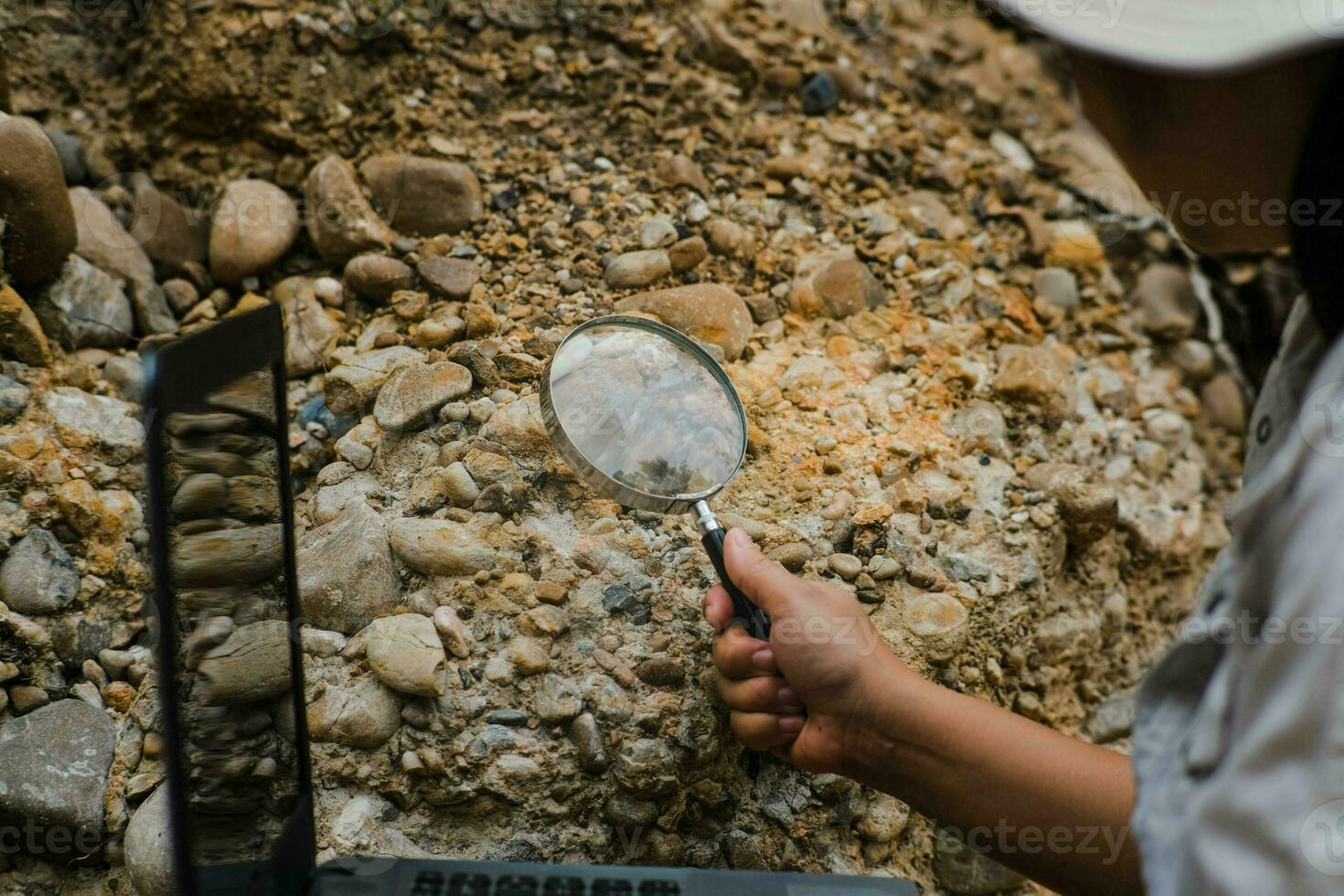 Close-up of female geologist using magnifying glass to examine and analyze rock, soil, sand in nature. Archaeologists explore the field. Environmental and ecology research. photo