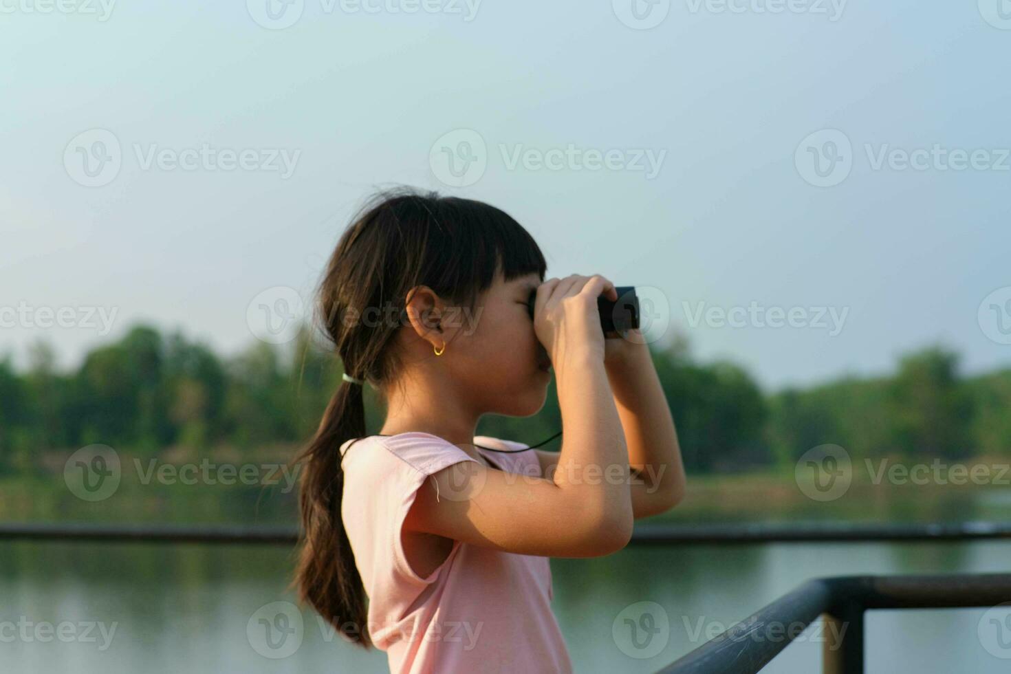 Little girl looking through binoculars at birds on the reservoir. Explore and adventure concept. Birdwatching photo