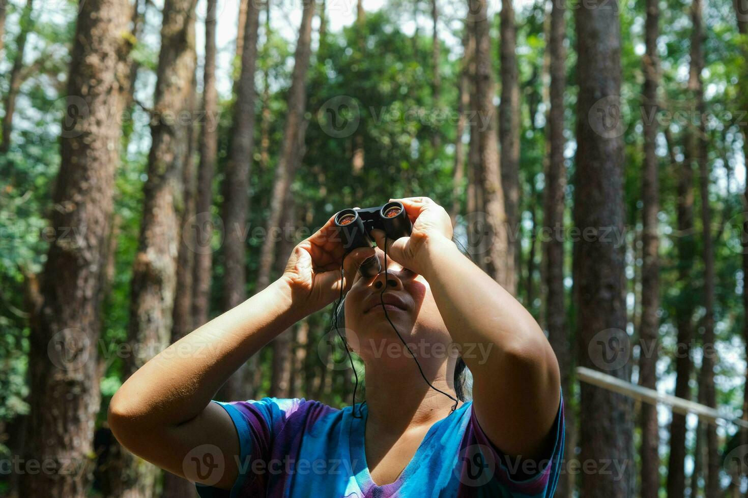 Young woman looking at birds in the forest through binoculars. Female tourist with tool watching the nature in forest. Healthy lifestyle and eco-tourism. photo