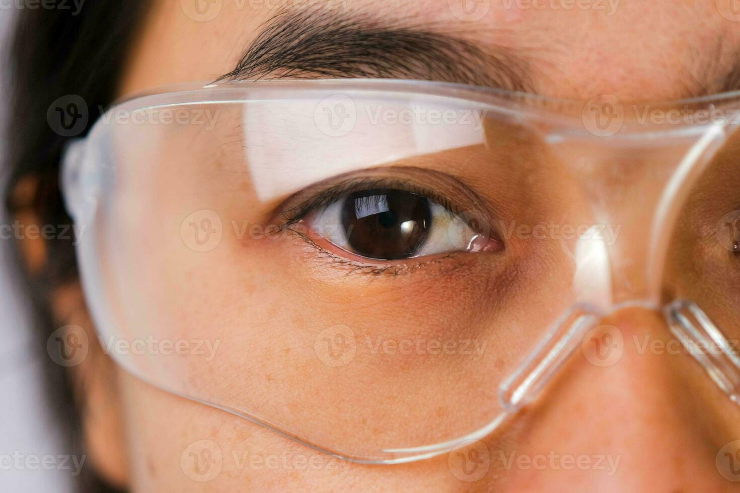 Close-up of woman's eye wearing transparent safety glasses. Asian woman wearing protective goggles. photo