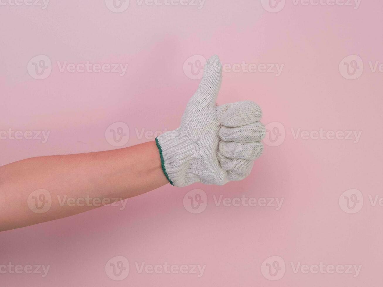 Hands in white knitted gloves isolated on pink background. Female hand showing thumb up with cotton gloves. photo