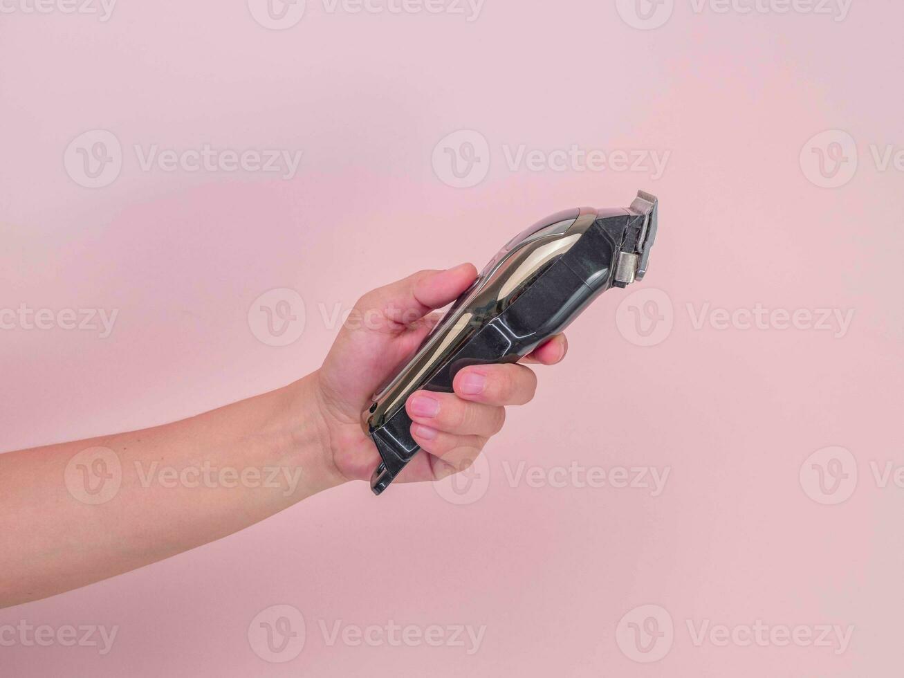 Close up hand holding electric hair clipper on pink background. Haircutting machine in hand. photo