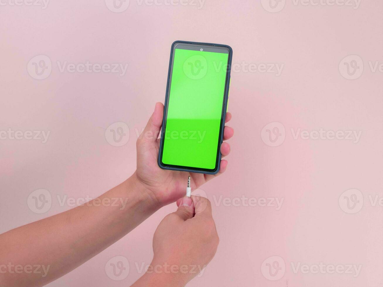 Female hands plugging earphone into smart phone with green screen isolated on pink background. Close-up of hand plugging in headphone device in smartphone. photo