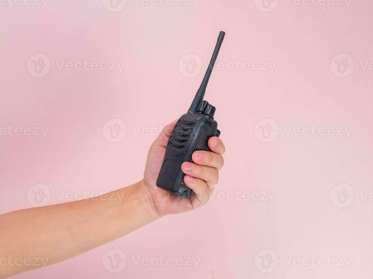 Close up hand holding portable walkie talkie isolated on pink background. Black handheld walkie talkie photo