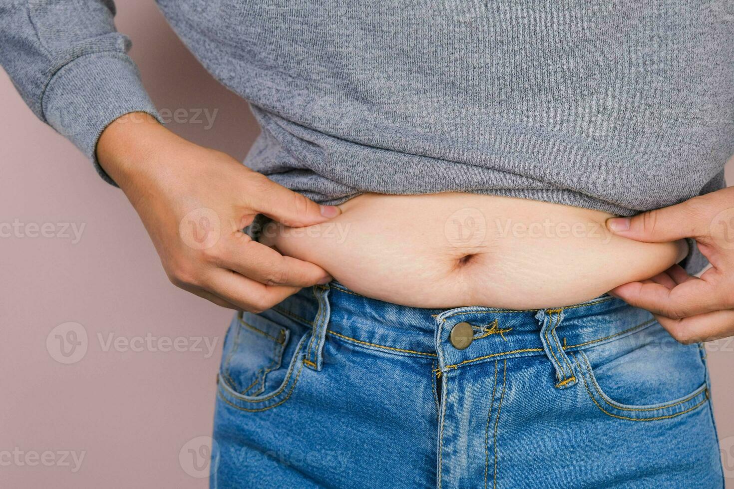 Fat woman hand holding excessive belly fat isolated on pink background. Overweight fatty belly of woman. Female diet and body health care concept photo