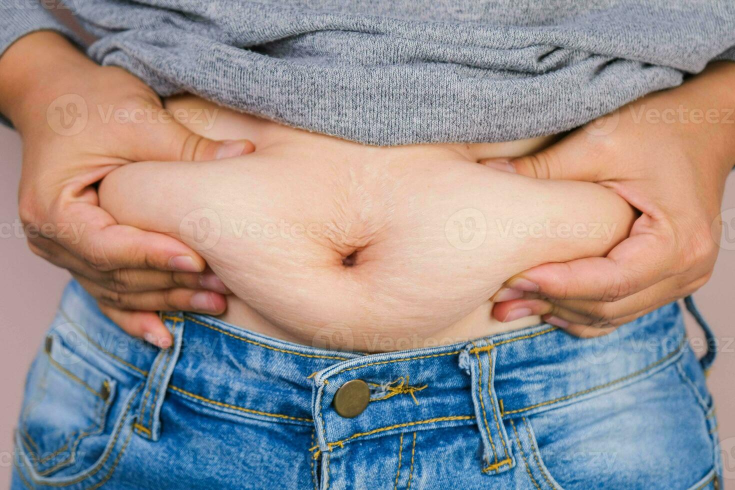 Fat woman hand holding excessive belly fat isolated on pink background. Overweight fatty belly of woman. Female diet and body health care concept photo