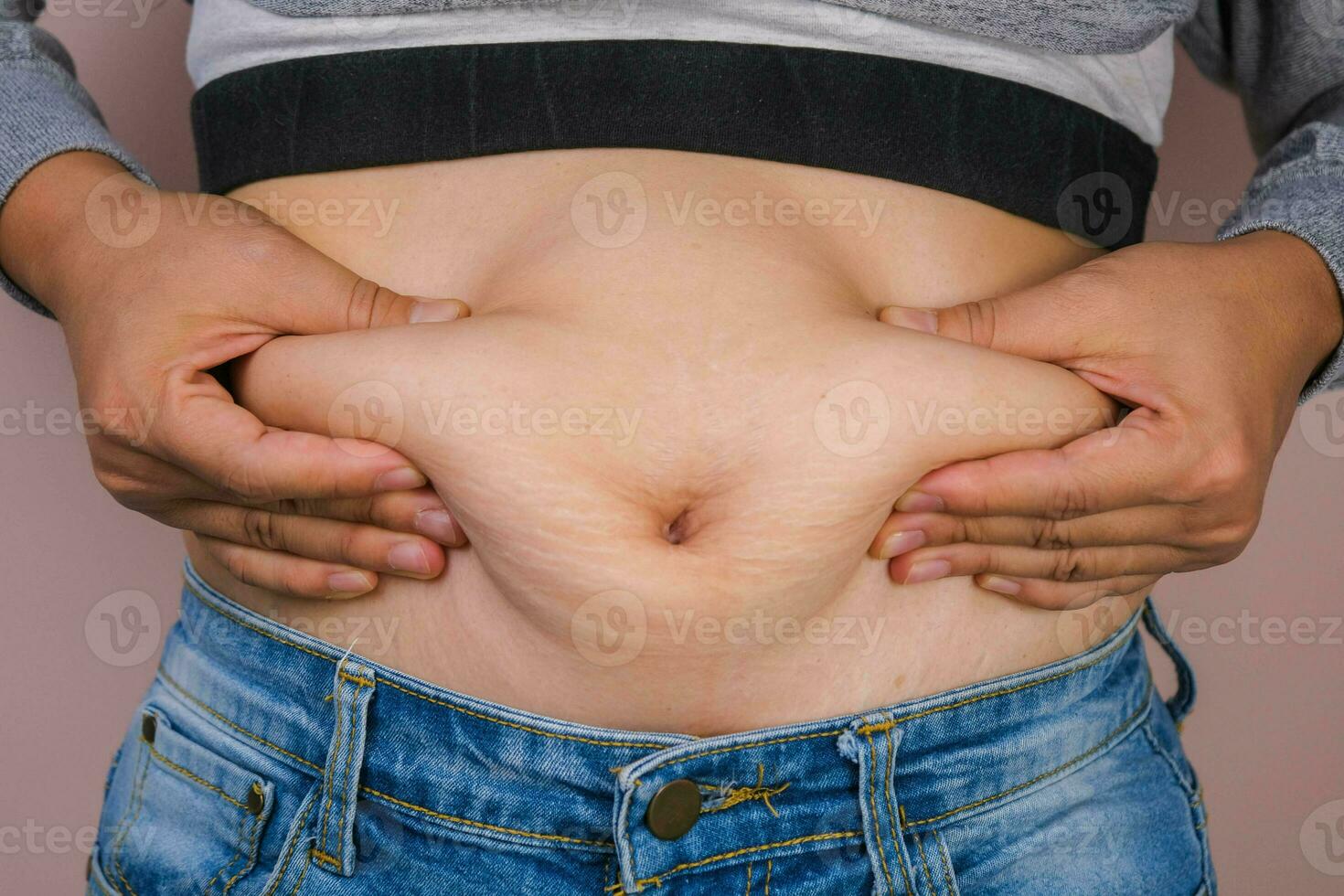 Fat woman hand holding excessive belly fat isolated on pink background. Overweight fatty belly of woman. Female diet and body health care concept photo