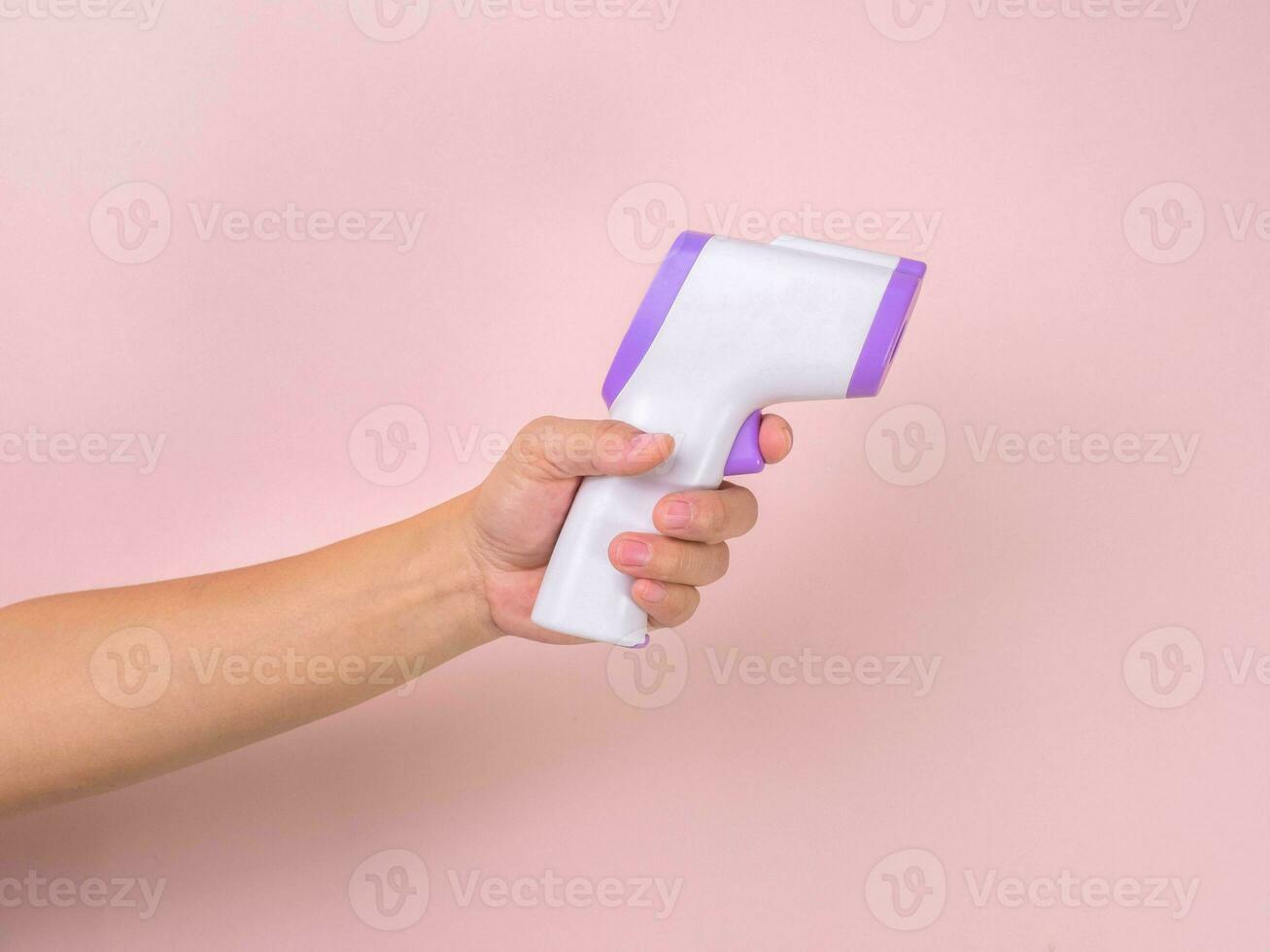 Close up of hand holding Digital Thermometer thermometer gun Medical Thermometer Non Contact Infrared Sight Handheld Reading Forehead. Temperature Measurement Device isolated on pink background. photo