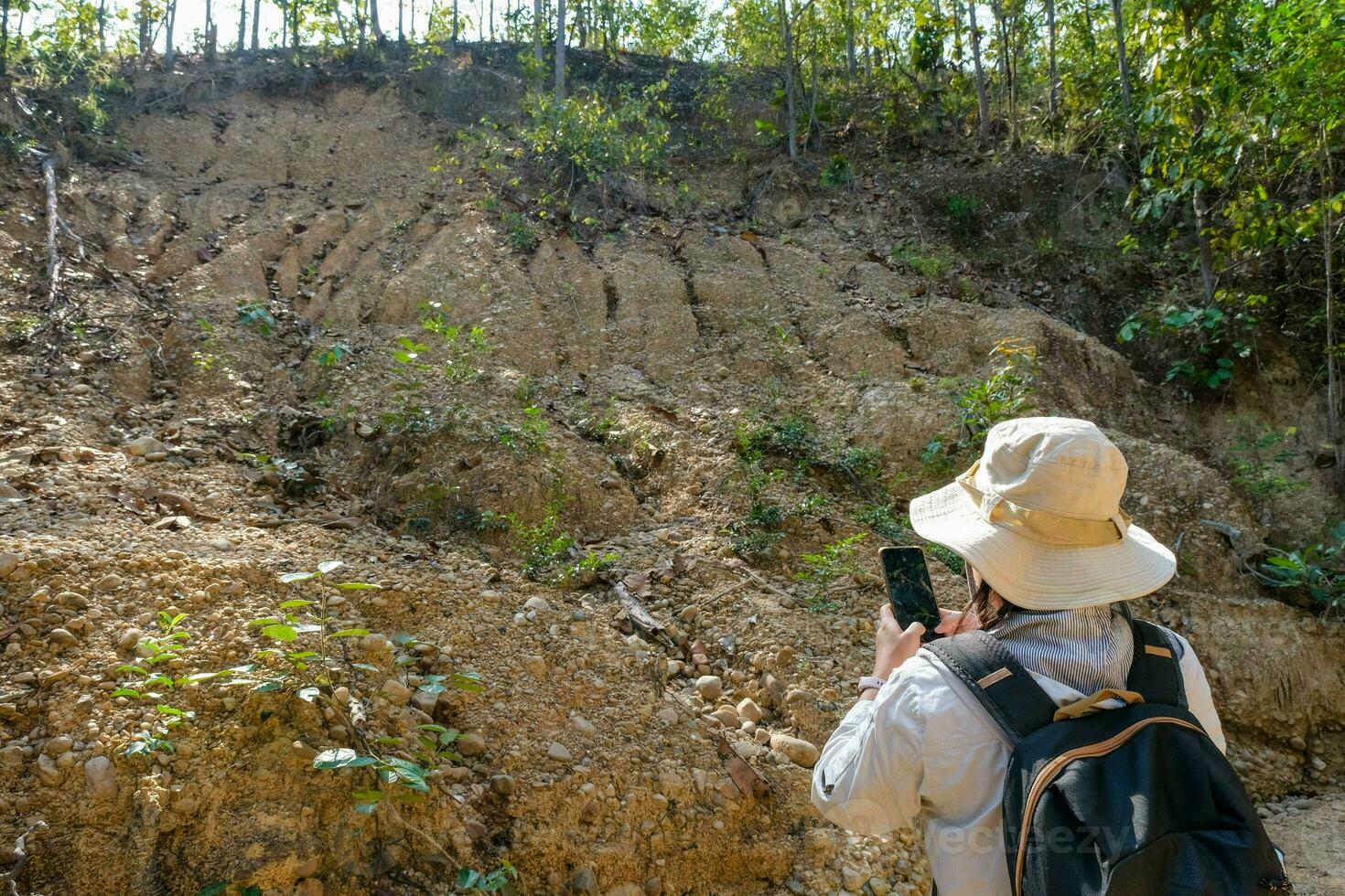 Female geologist using mobile phone inspecting nature, analyzing rocks or pebbles. Researchers collect samples of biological materials. Environmental and ecology research. photo