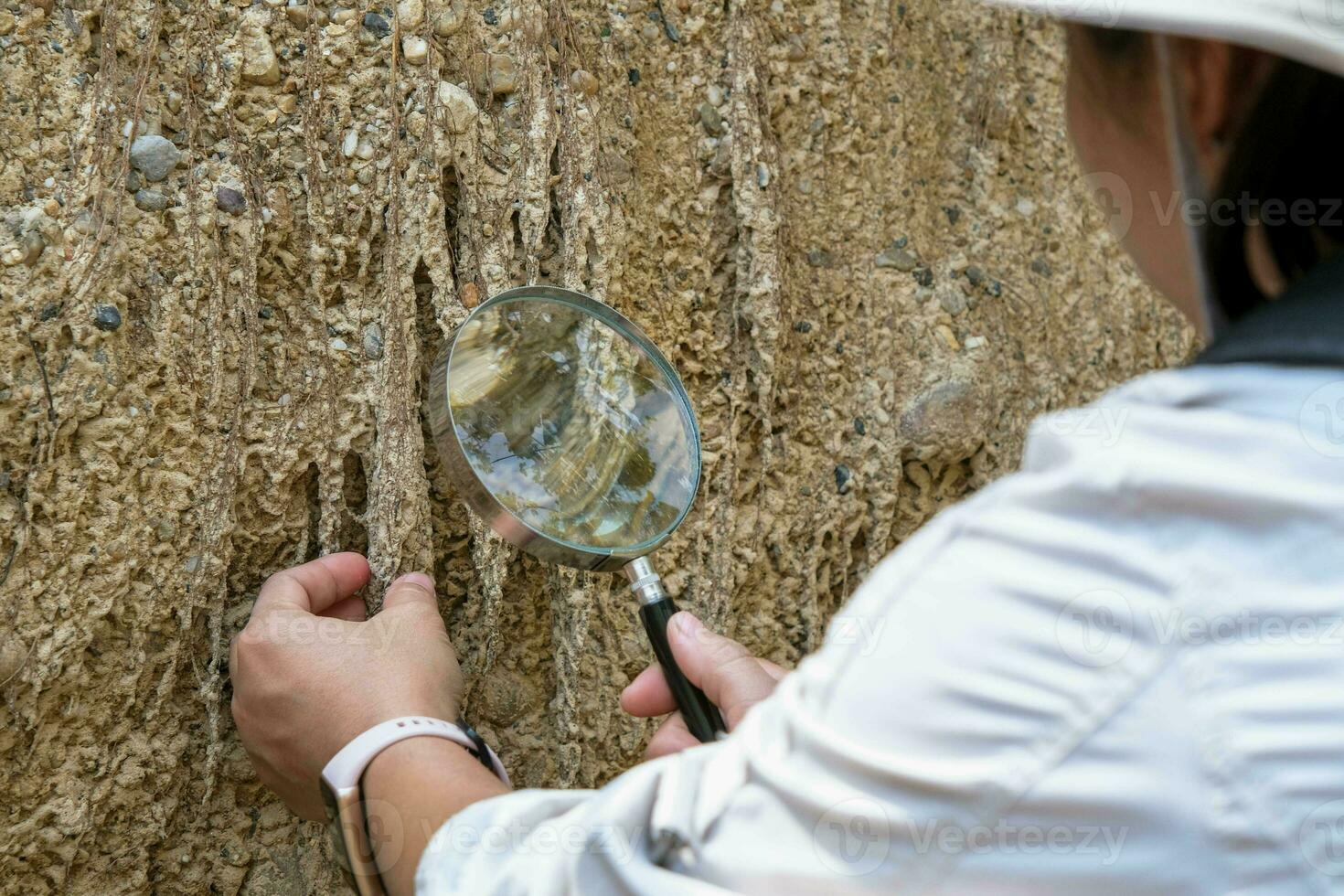 Female geologist using a magnifying glass examines nature, analyzing rocks or pebbles. Researchers collect samples of biological materials. Environmental and ecology research. photo