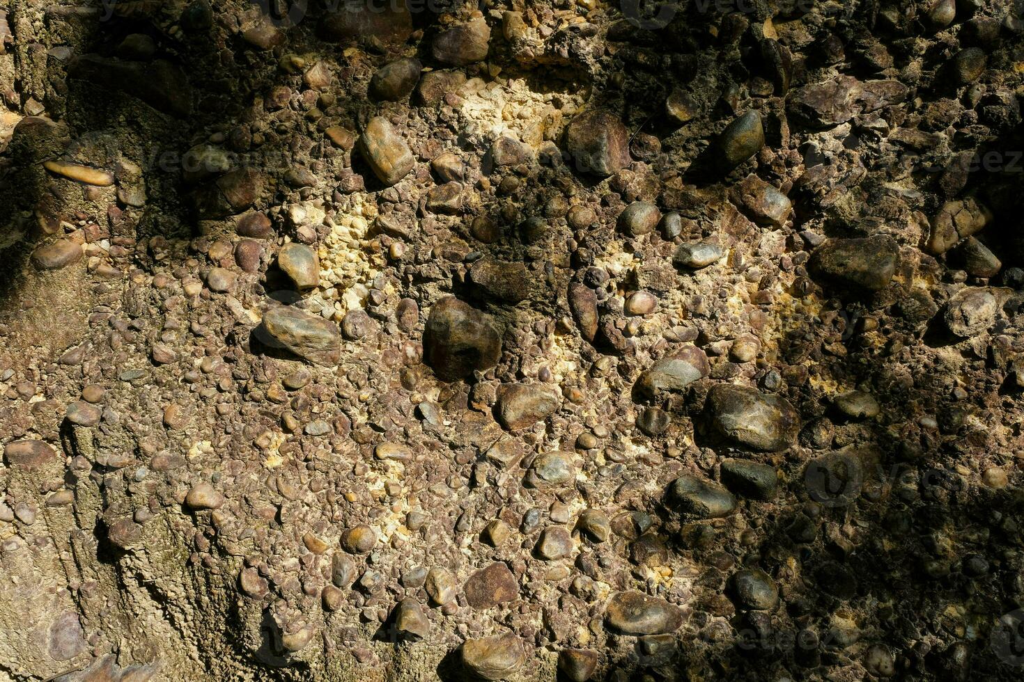 cerca arriba de el acantilado Roca superficie, un natural fenómeno causado por el erosión de el sedimento ese fluye a lo largo el corriente de agua, formando un sedimentario capa con redondeado río rocas incrustado en él. foto