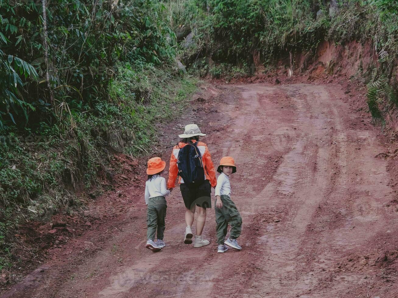 Happy young woman with her daughter walking on a field trip together in the mountains. Family on a hiking adventure through the forest. Parents teach their children about nature and plants. photo