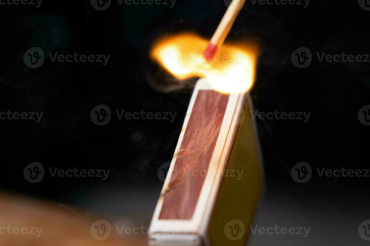 Matchstick fires on matchbox in slow motion close-up. The match was being lit, a blazing fire. Shot of igniting match against black Background. photo
