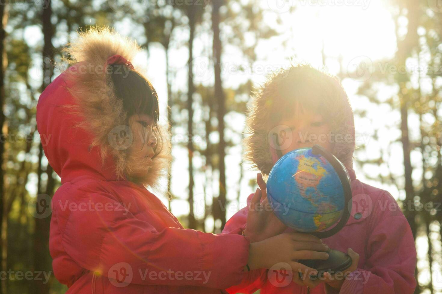 Two cute Asian girls learning a model of the world on nature background and warm sunlight in the park. Children learn through educational play activities. Earth day. World environment day. photo