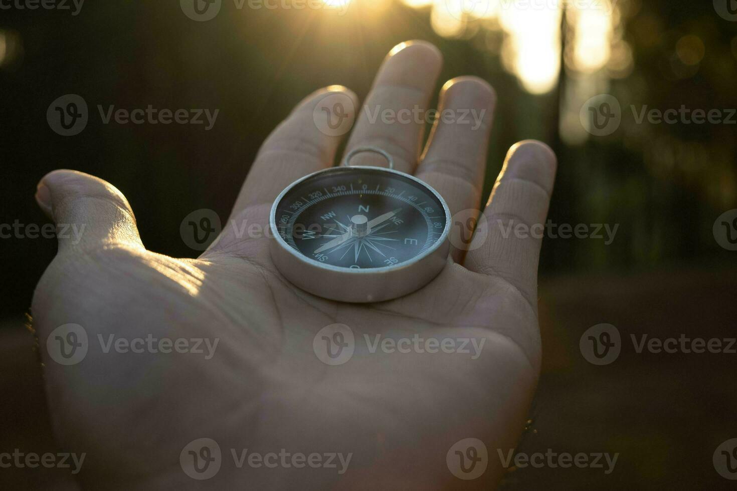 Compass in hand on natural pine forest background. hand holding compass in forest landscape. Young traveler searching direction with compass in summer mountains. photo