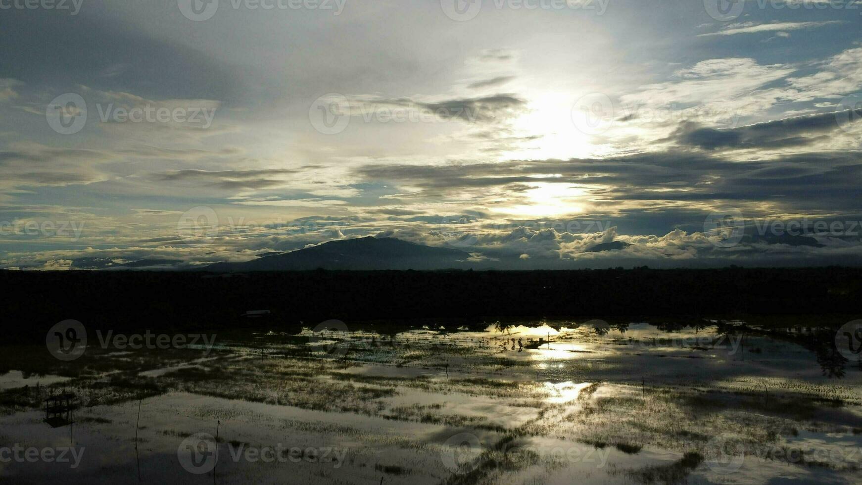 Aerial view of the flooded agricultural fields against the background of the shadows of the mountains and the overcast sky at dusk. Beautiful nature of storm clouds in the daytime. photo