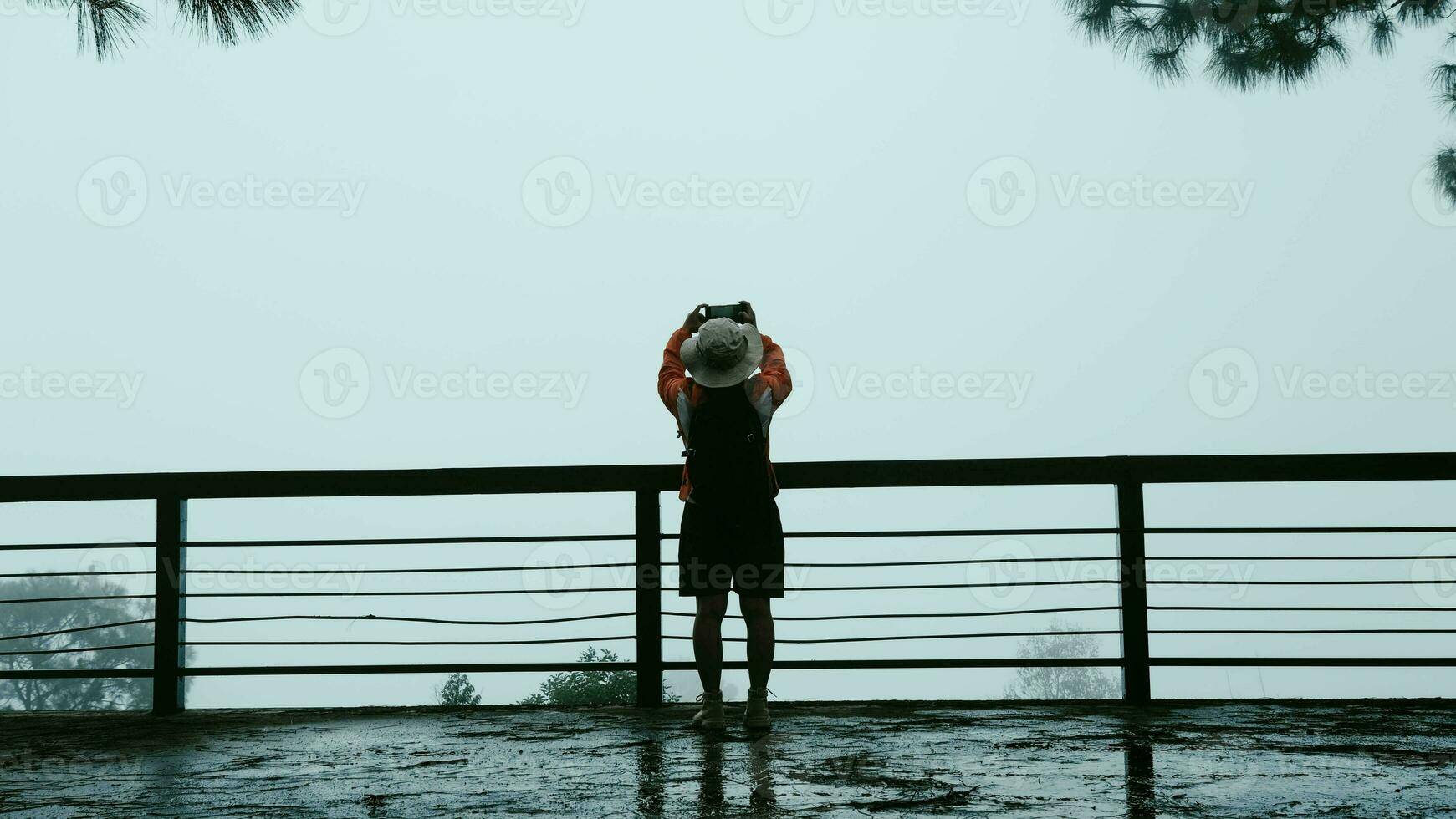 posterior ver de un joven mujer con un mochila en pie en un calma montaña parte superior y tomando imágenes de el hermosa montaña paisaje de el Mañana niebla en el teléfono. foto