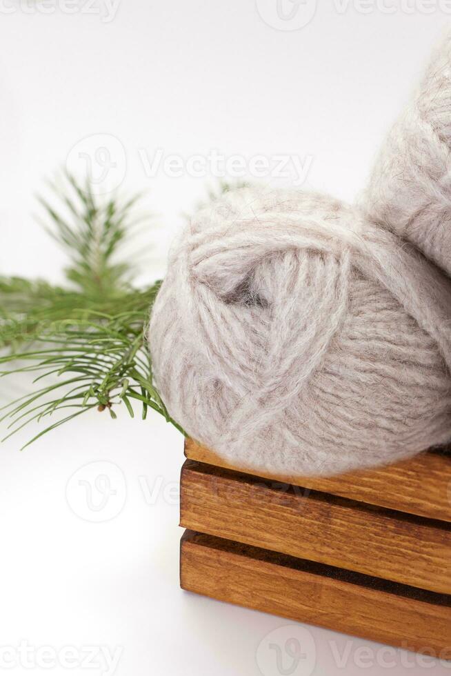 Gray wool skeins or yarn in brown box with spruce branch on white background. Handmade, knitting, hobby. Copy space photo