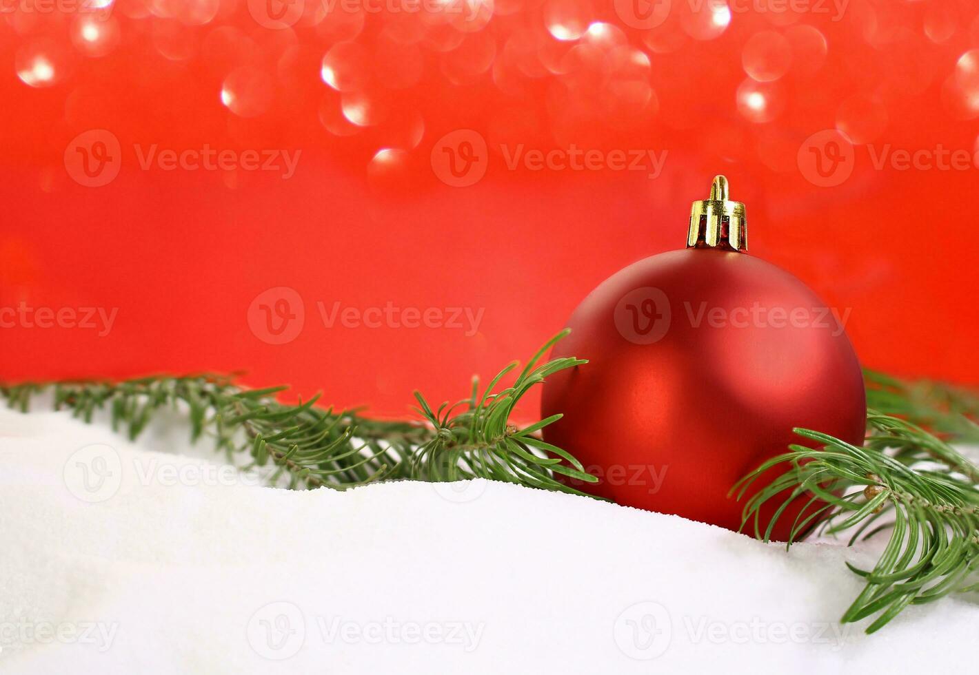 Red shiny ball on snow with  pine branch with blurred bokeh on red background. Christmas, New Year. Copy space photo
