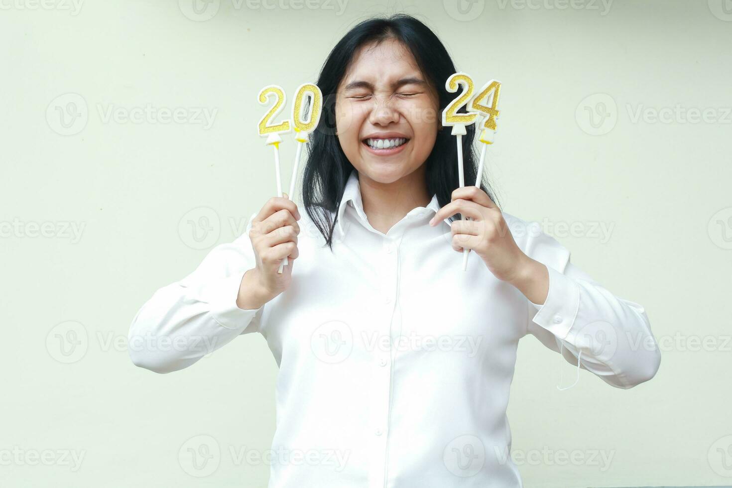 beautiful asian young woman excited for 2024 new years celebration by holding golden numbers candles and close eyes wear white shirt formal isolated photo