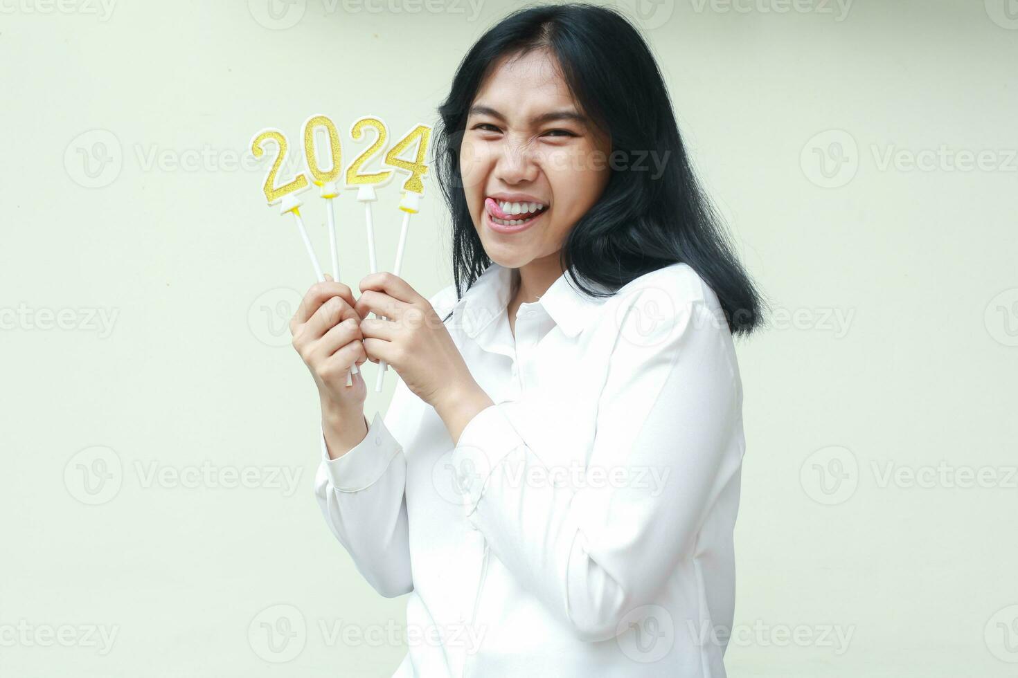 successful asian coworker excited to celebrate 2024 new years by holding numbers golden candles on her hand wearing formal white shirt smiling at camera isolated photo