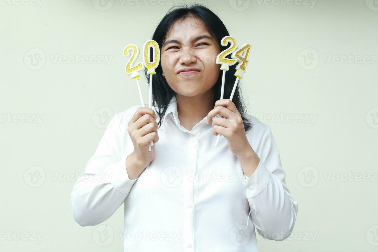asiático oficina trabajador joven mujer emocionado a celebrando 2024 nuevo años víspera por participación número reluciente dorado velas vestir blanco formal traje mirando lejos aislado foto