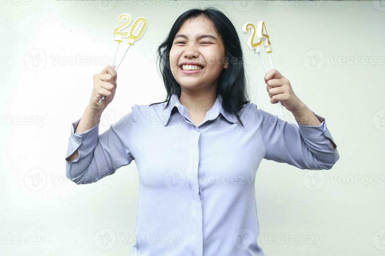 cheerful asian young woman holding candles number 2024 to celebrate new years eve party wearing grey shirt photo