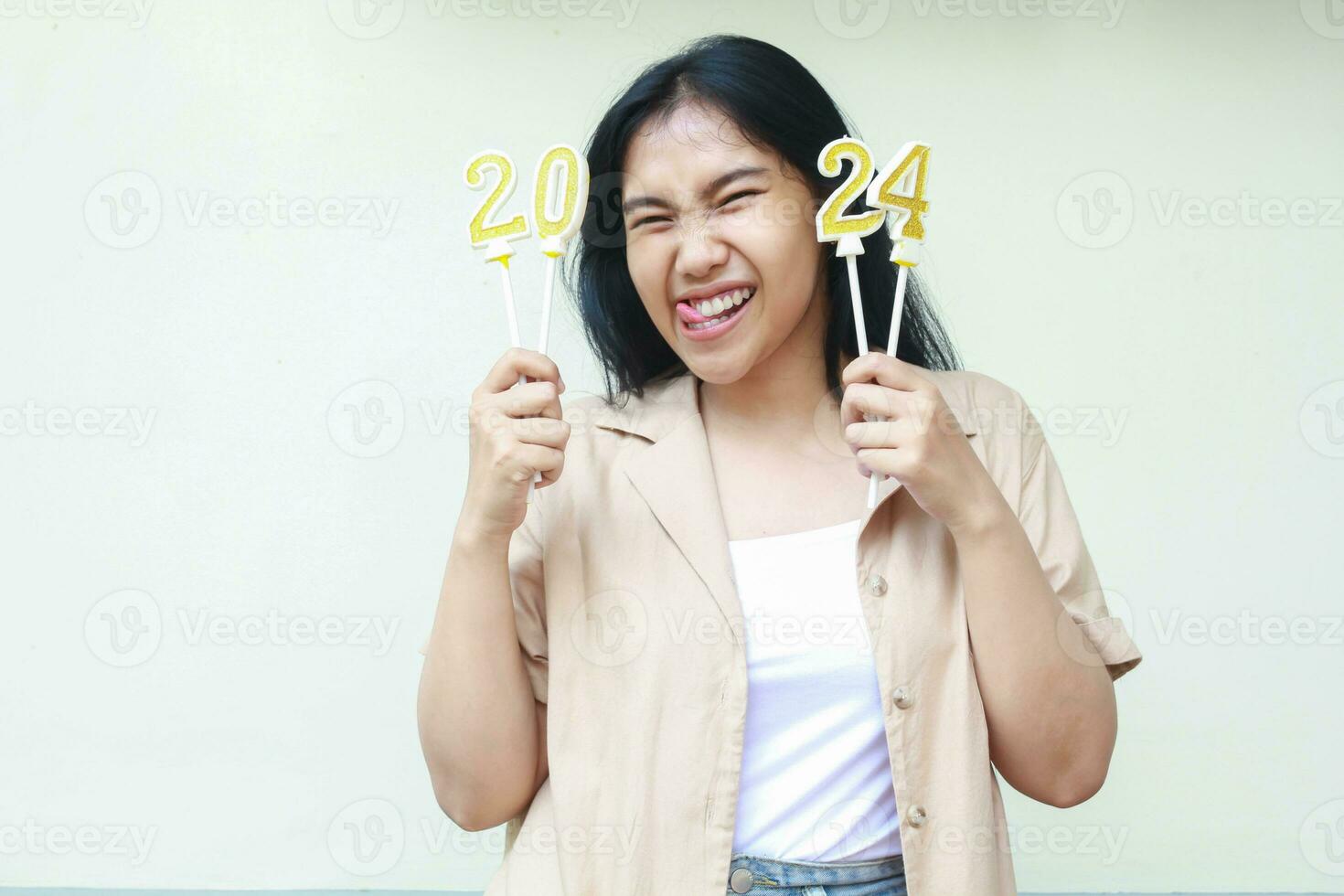 excited asian young business woman celebrate new years eve by holding golden candles numbers 2024 wear casual brown clothes looking at camera isolated on white background photo