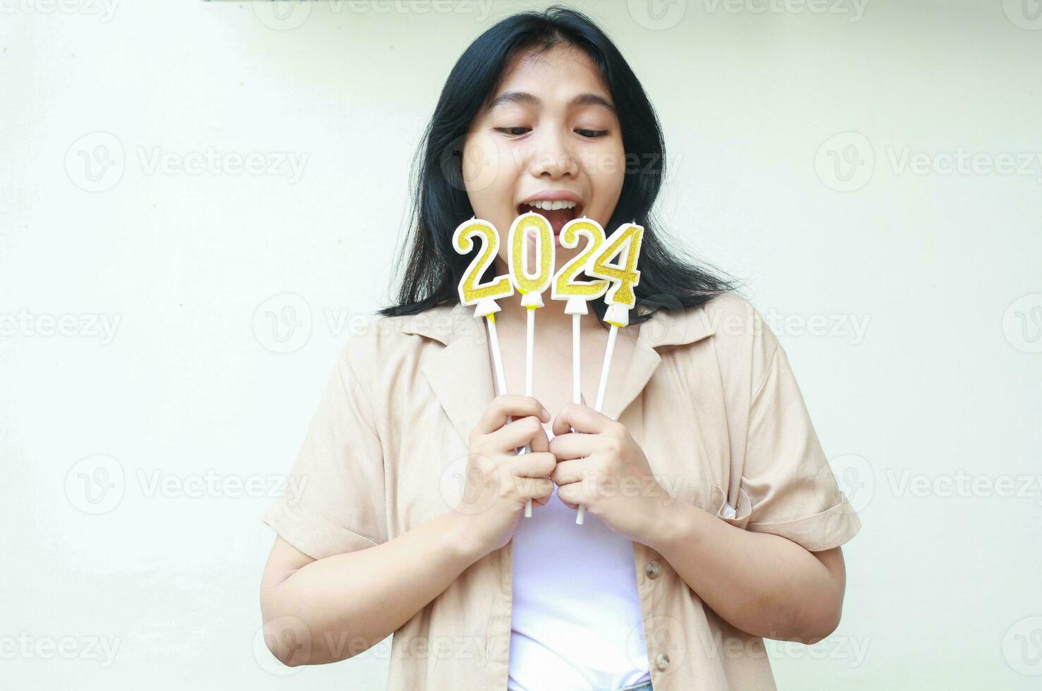 excited young woman indonesian holding gold candles numbers 2024 to celebrating new years eve wear casual brown shirt looking down isolated on white background photo