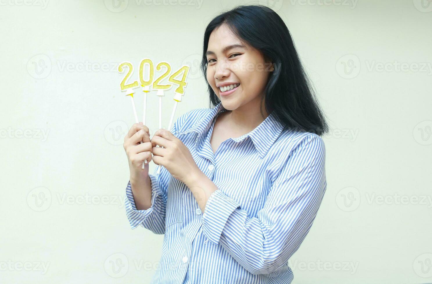 retrato de emocionado asiático joven negocio mujer participación dorado velas números 2024 para nuevo años víspera celebracion vistiendo tira azul camisa mirando a cámara aislado en blanco antecedentes foto